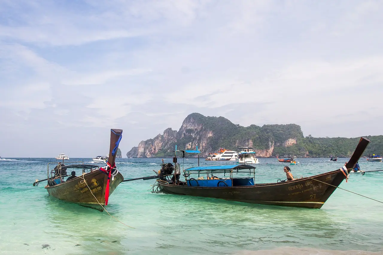 Longtail boats at Monkey Beach on Phi Phi Don with limestone cliffs across the water