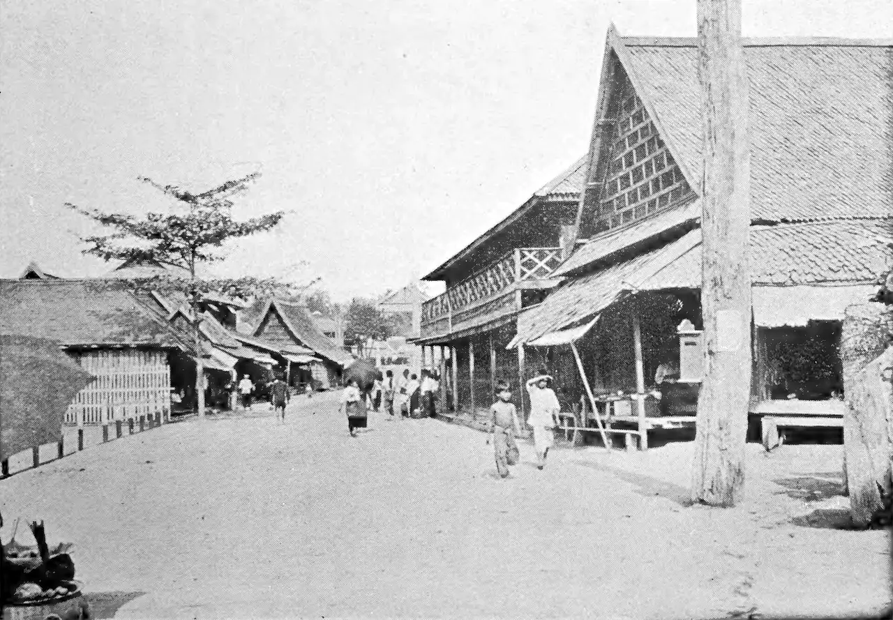 ถนนสายหนึ่งในเมืองแพร่ในภาพถ่ายเก่า มีเรือนแถวไม้และผู้คนเดินอยู่