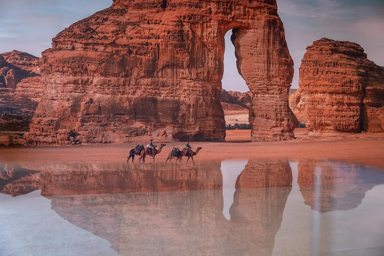 Elephant Rock หรือ Jabal AlFil ที่อัลอูลา มีน้ำขังสะท้อนภาพและมีอูฐเดินอยู่ ภาพปี 2567 ของ Saudi Press Agency จาก Wikimedia Commons สัญญา CC BY-SA 4.0