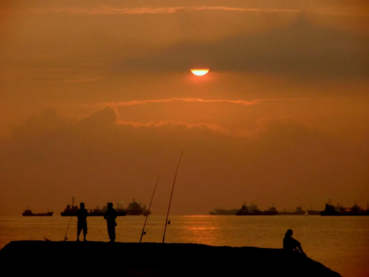 ตกปลาริมโขดหินยามอาทิตย์ขึ้นที่ East Coast Park เห็นเรือสินค้าไกล ๆ ภาพจาก Wikimedia Commons ผู้ถ่าย Adhirk สัญญา CC BY-SA 3.0 ถ่ายปี 2552