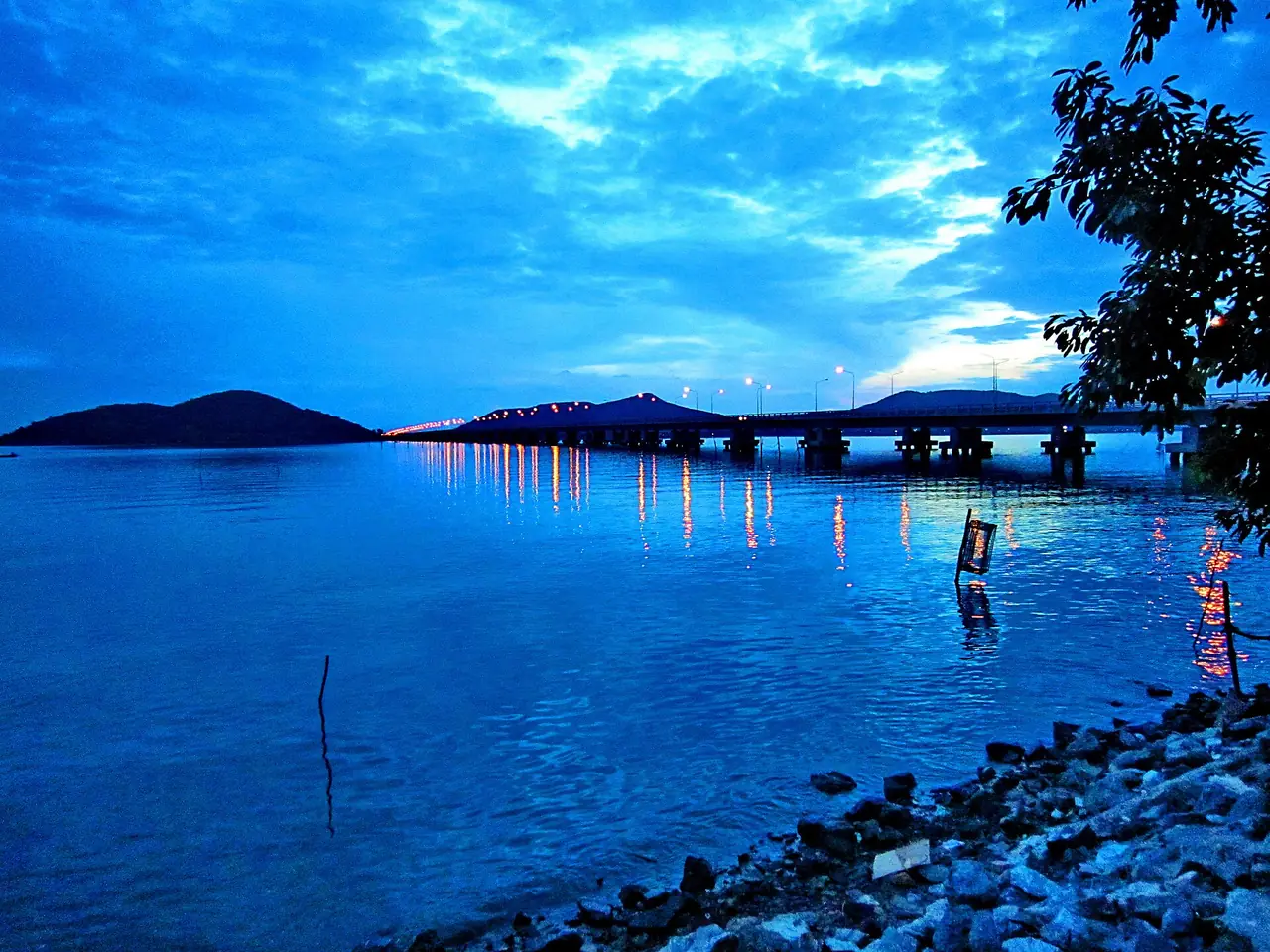 สะพานติณสูลานนท์ยามพลบค่ำ ไฟบนสะพานสะท้อนผิวน้ำ ภาพของผู้ใช้ ::::=UT=:::: จาก Wikimedia Commons (CC BY-SA 3.0)