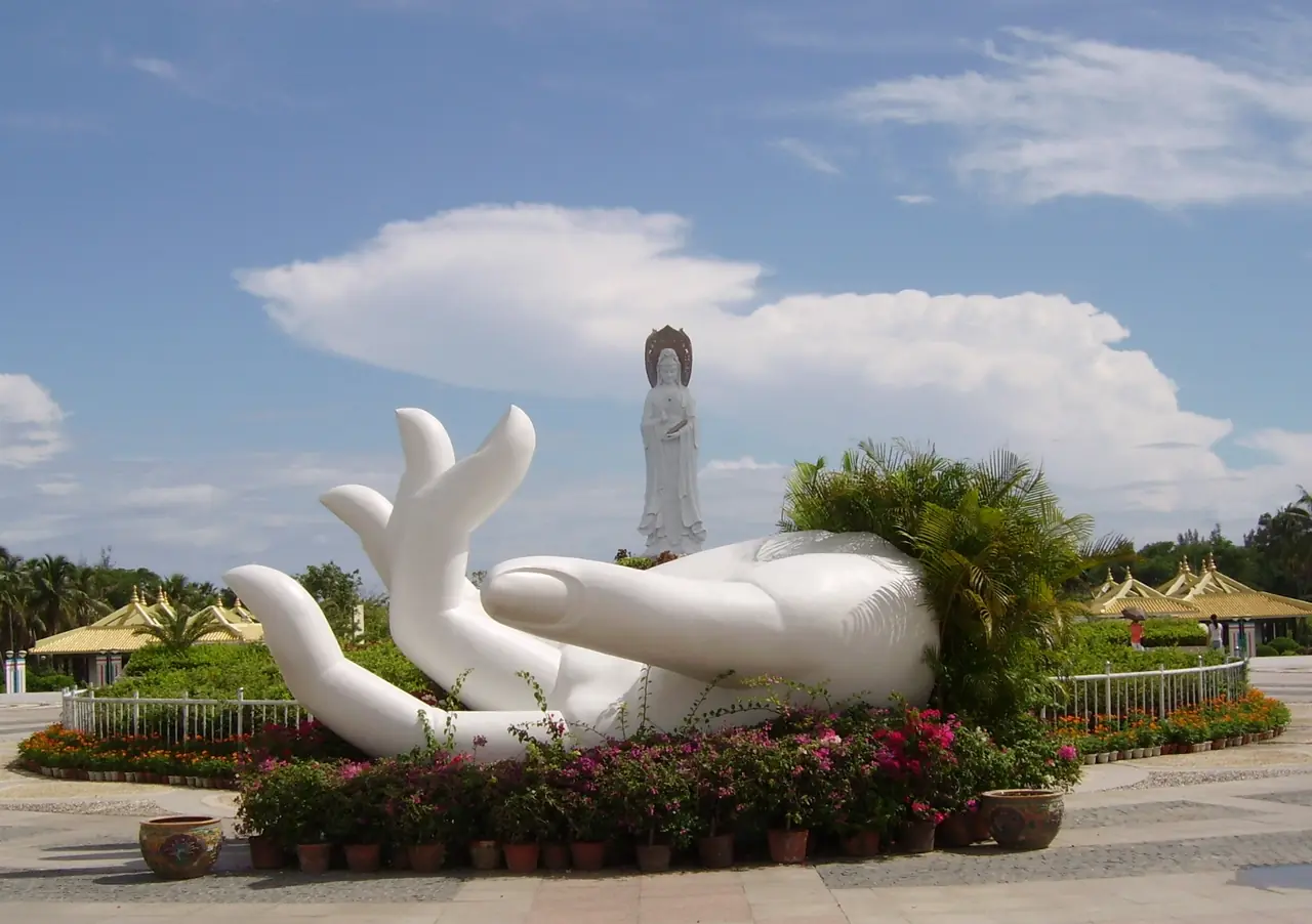 ลานทางเข้ามีประติมากรรมฝ่ามือสีขาวขนาดใหญ่ และเห็นรูปกวนอิมไกล ๆ ภาพจากคอมมอนส์
