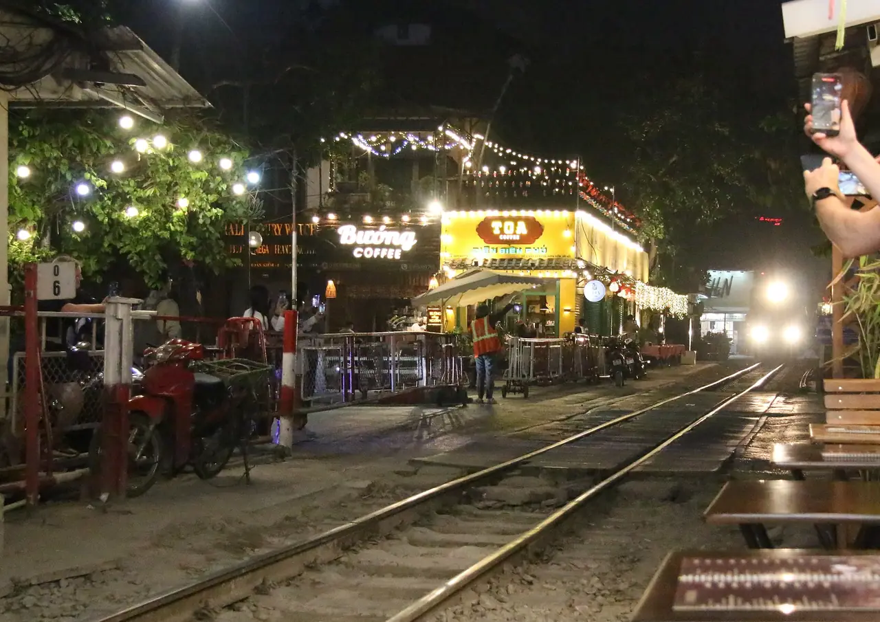 ร้านกาแฟริมรางตอนค่ำ ไฟประดับ และแสงไฟหน้ารถไฟด้านขวา