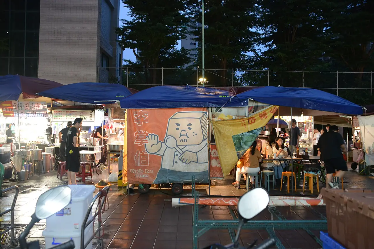 แผงอาหารใต้หลังคาผ้าใบสีน้ำเงินในตลาดหนิงเซี่ย มีโต๊ะนั่งกินหน้าร้าน ภาพเดือน ส.ค. 2569 จาก Wikimedia Commons ผู้ถ่าย Jonashtand สัญญา CC BY-SA 4.0