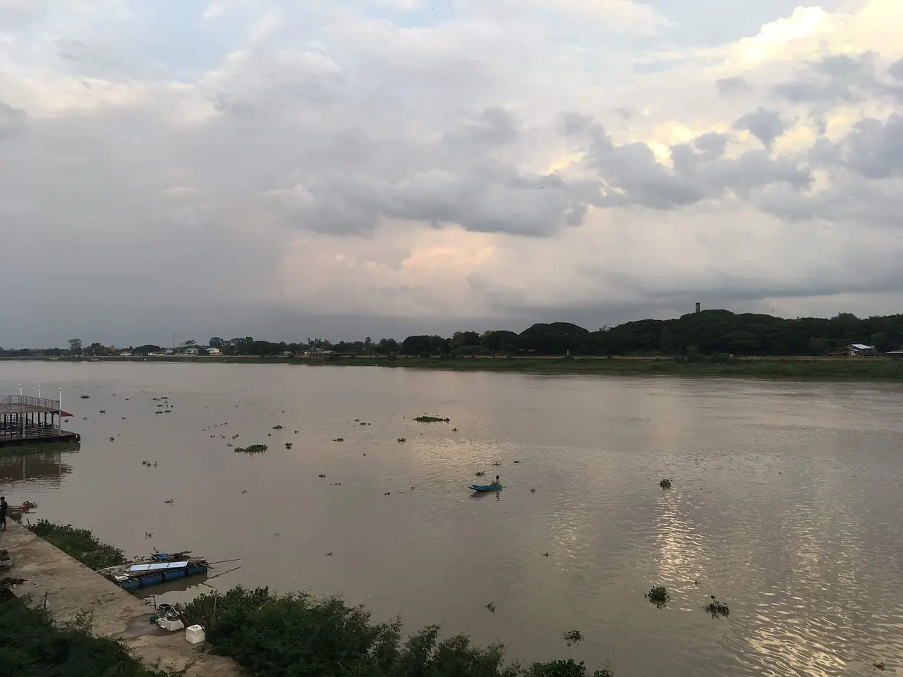แม่น้ำมูลที่อุบลราชธานีใต้ท้องฟ้าหม่น มีแนวต้นไม้ริมฝั่งตรงข้าม
