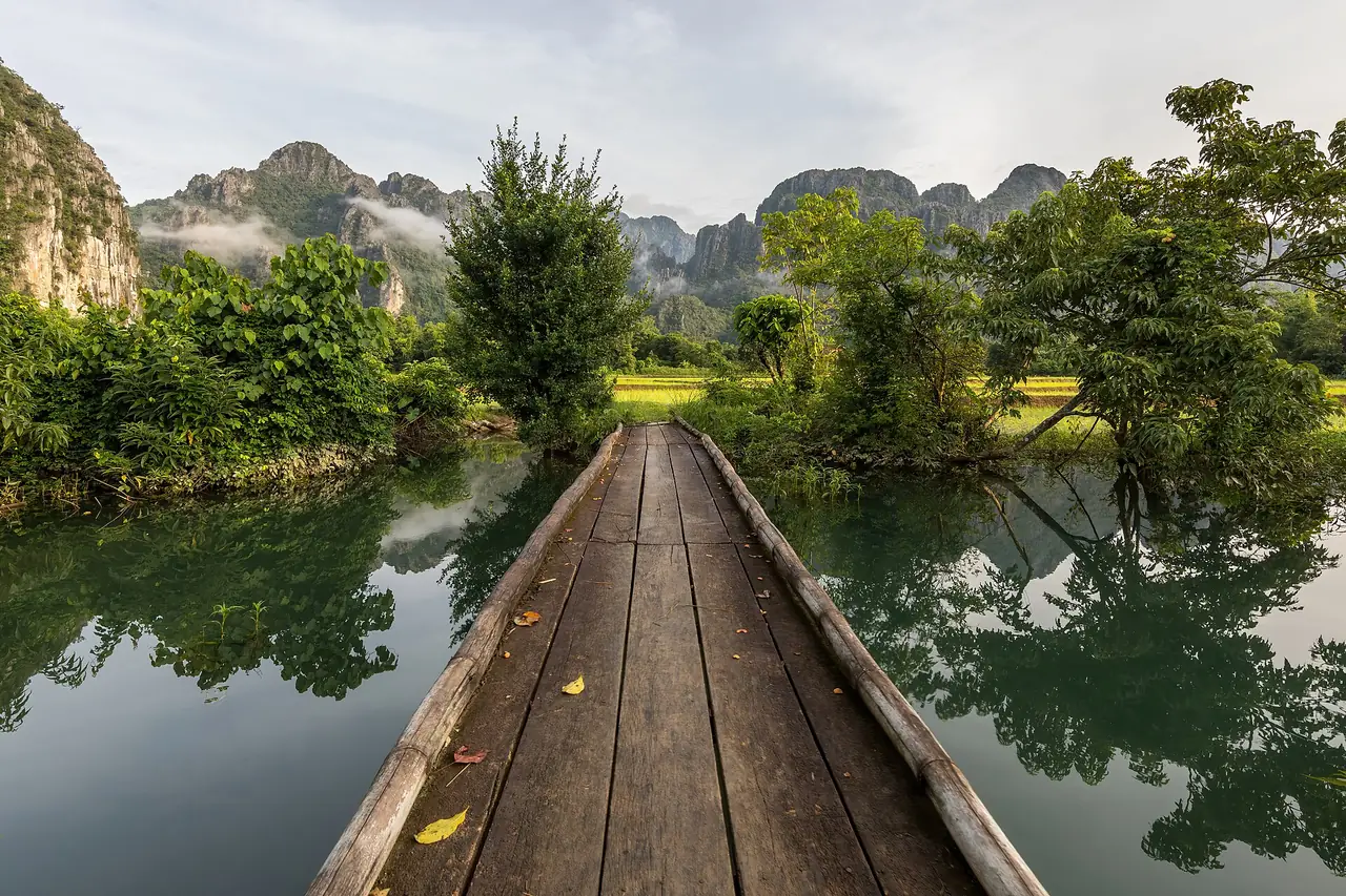 สะพานไม้ข้ามบ่อน้ำในทุ่งนาใกล้เมืองวังเวียง ภาพช่วงเช้าตรู่ (ภาพบรรยากาศ ไม่ใช่บ่อใดโดยเฉพาะ)