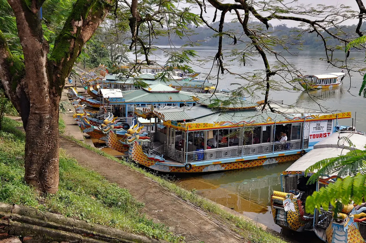 เรือมังกรรับนักท่องเที่ยวจอดเรียงริมแม่น้ำหอม ภาพจาก Wikimedia Commons ผู้ถ่าย P. Hughes สัญญา CC BY 4.0