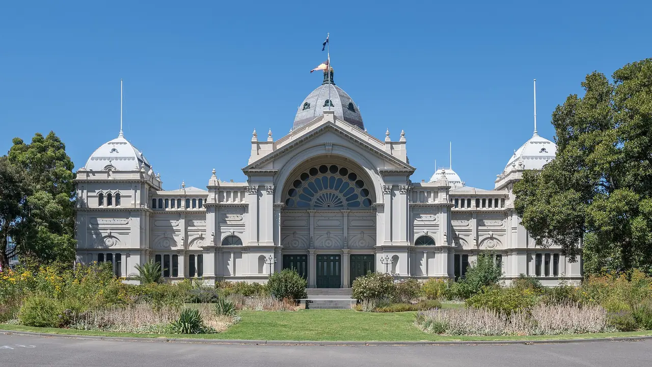 อาคาร Royal Exhibition Building และสวน Carlton Gardens เมลเบิร์น มองจากทิศตะวันตก ภาพจาก Wikimedia Commons ผู้ถ่าย DXR สัญญา CC BY-SA 4.0 ถ่ายปี 2023