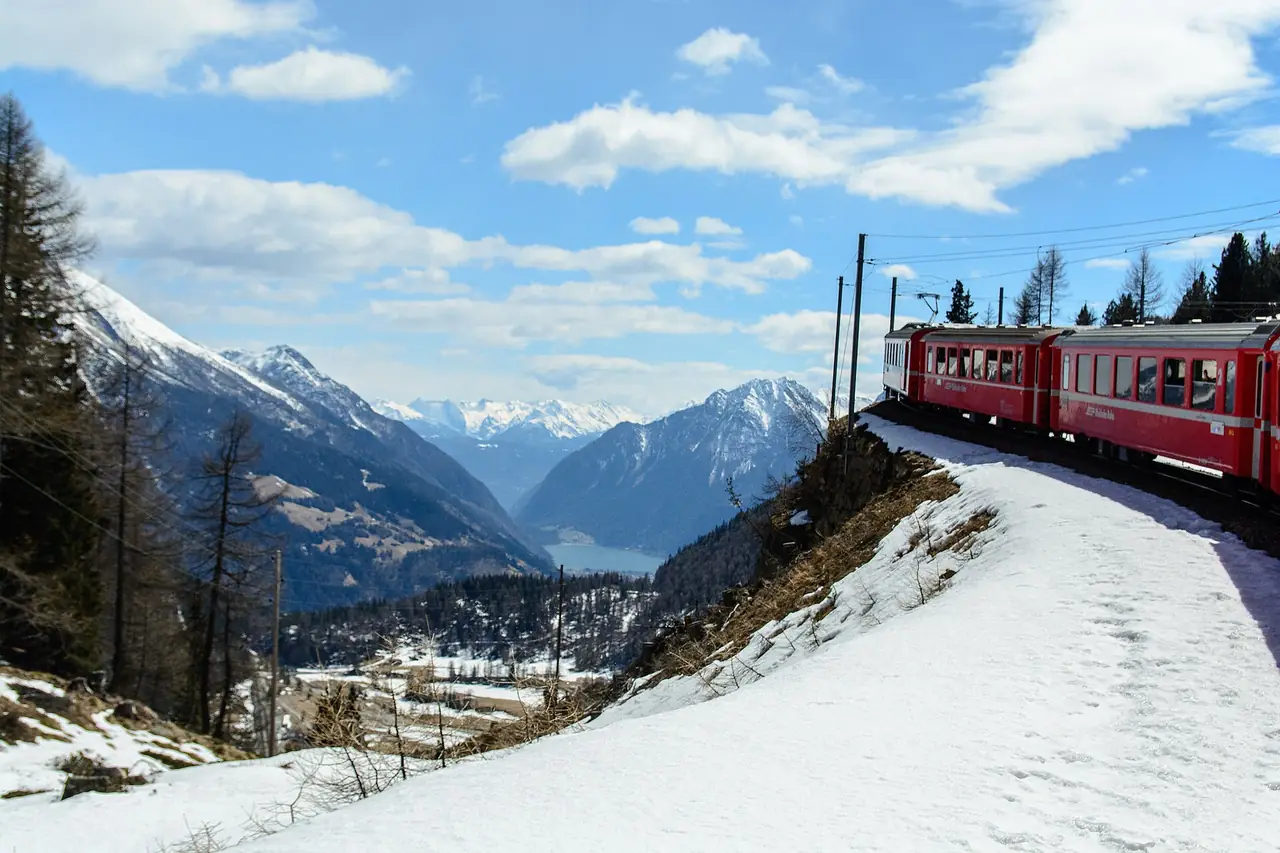 ขบวน RhB บนทางลาดหิมะมองเห็นทะเลสาบ Poschiavo ภาพจาก Wikimedia Commons ผู้ถ่าย Etsius สัญญา CC BY-SA 4.0 ไม่ทราบวันที่ถ่าย เป็นภาพต้นฤดูใบไม้ผลิหรือหน้าหนาว