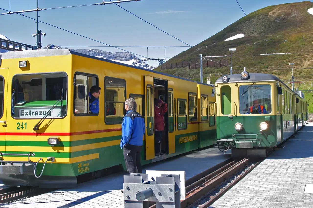 รถไฟรางฟันเฟือง Wengernalpbahn สีเขียวเหลืองที่ชานชาลา ภาพจาก Wikimedia Commons ผู้ถ่าย W. Bulach สัญญา CC BY-SA 4.0 ไม่ทราบปีที่ถ่ายและชื่อสถานี