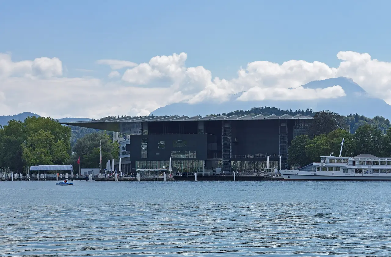 อาคาร KKL ริมทะเลสาบลูเซิร์นที่มีพิพิธภัณฑ์ศิลปะอยู่ภายใน ภาพจาก Wikimedia Commons ผู้ถ่าย Ymblanter สัญญา CC BY-SA 4.0 ไม่ทราบปีที่ถ่าย เป็นภาพประกอบ มีเรือโดยสารจอดข้างอาคาร