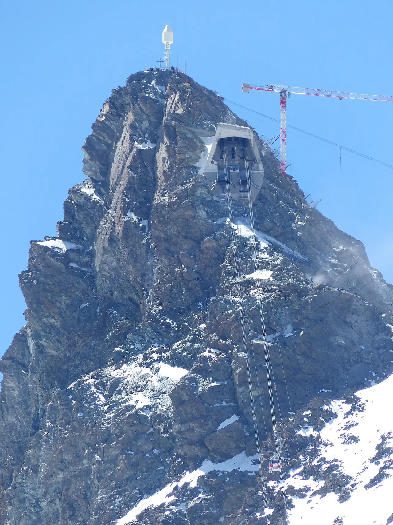 ยอดสถานีกระเช้า Klein Matterhorn ที่ปลายยอดเขา มีเครนก่อสร้างอยู่ด้านข้าง ภาพจาก Wikimedia Commons ผู้ถ่าย Whgler สัญญา CC BY-SA 4.0 ไม่ทราบปีที่ถ่ายและเป็นภาพช่วงก่อสร้าง ไม่ใช่สภาพปัจจุบัน