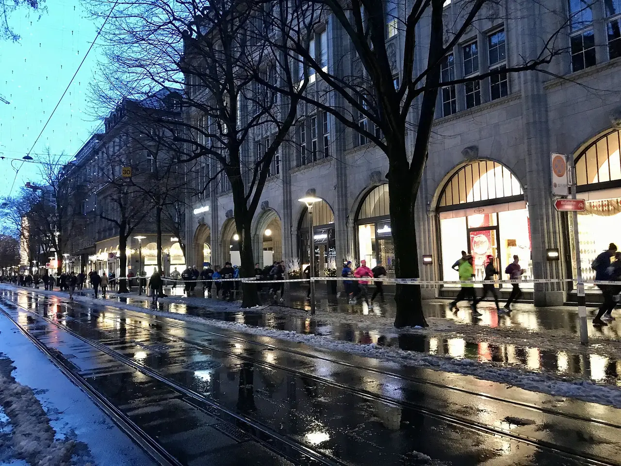 ถนน Bahnhofstrasse ตอนเย็นหน้าหนาว มีรางรถรางและผู้คนวิ่งออกกำลังกายริมถนน ภาพจาก Wikimedia Commons ผู้ถ่าย Ank Kumar สัญญา CC BY-SA 4.0 ไม่ทราบวันที่ถ่าย เป็นภาพประกอบ