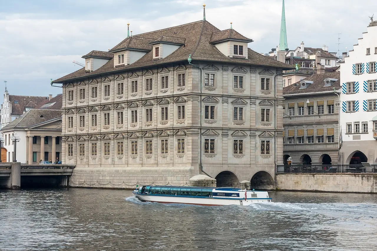 ศาลาว่าการเมืองซูริก (Rathaus) ริมแม่น้ำ Limmat มีเรือโดยสารแล่นผ่าน ภาพจาก Wikimedia Commons ผู้ถ่าย JoachimKohler-HB สัญญา CC BY-SA 4.0 ไม่ทราบปีที่ถ่าย ชื่อเรือตามชื่อไฟล์