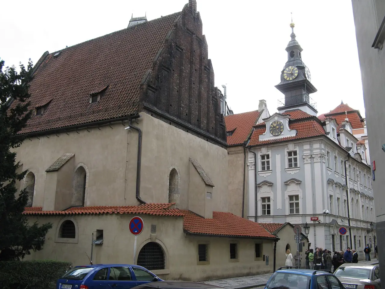 โบสถ์เก่า-ใหม่ (Old New Synagogue) หลังคาหน้าจั่วสูงชัดเจน และศาลาว่าการชาวยิวที่มีหอนาฬิกาอยู่ข้างๆ ภาพจาก Wikimedia Commons ผู้ถ่าย Yair Haklai สัญญา CC BY-SA 4.0