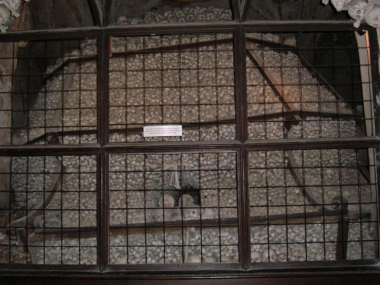 กะโหลกที่วางซ้อนกันหลังตะแกรงในโบสถ์กระดูก ภาพจาก Wikimedia Commons ผู้ถ่าย BrokenSphere สัญญา CC BY-SA 3.0 เป็นภาพเก่า ปัจจุบันห้ามถ่ายภาพ