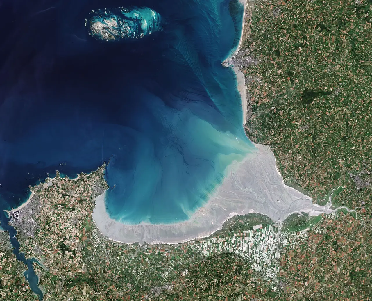 ภาพถ่ายดาวเทียม Copernicus Sentinel-2 ของอ่าวมงต์แซงต์มิเชลที่เห็นทรายเปิดตอนน้ำลง เป็นภาพมุมสูงเพื่ออธิบายพื้นที่อ่าวเท่านั้น ภาพจาก Wikimedia Commons ผู้ถ่าย European Space Agency สัญญา CC BY-SA 3.0 IGO