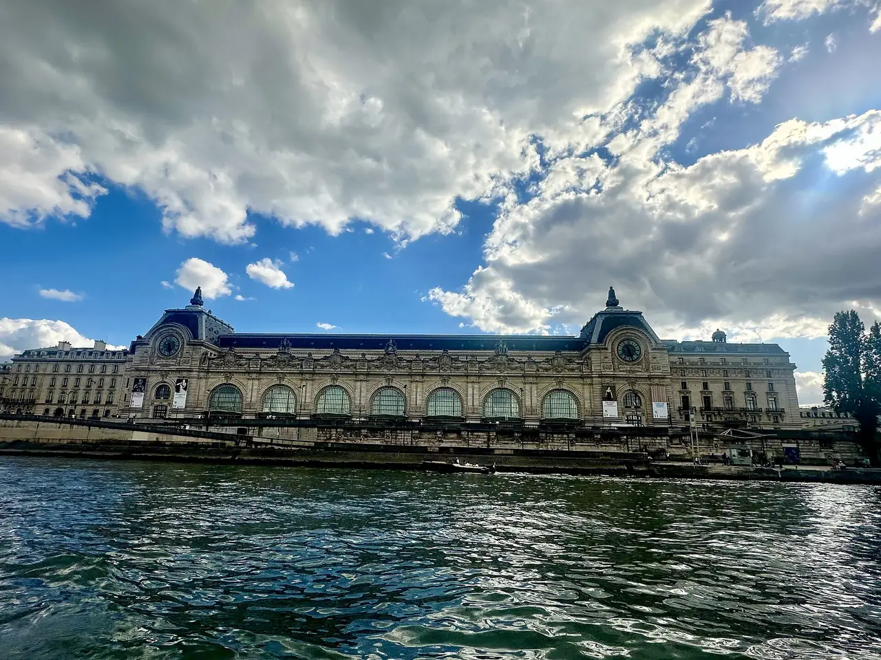 ด้านริมแม่น้ำของ Musée d'Orsay ที่มีหลังคาโค้งยาวและเมฆก้อนใหญ่ ภาพจาก Wikimedia Commons ผู้ถ่าย Richard N Horne สัญญา CC BY 4.0