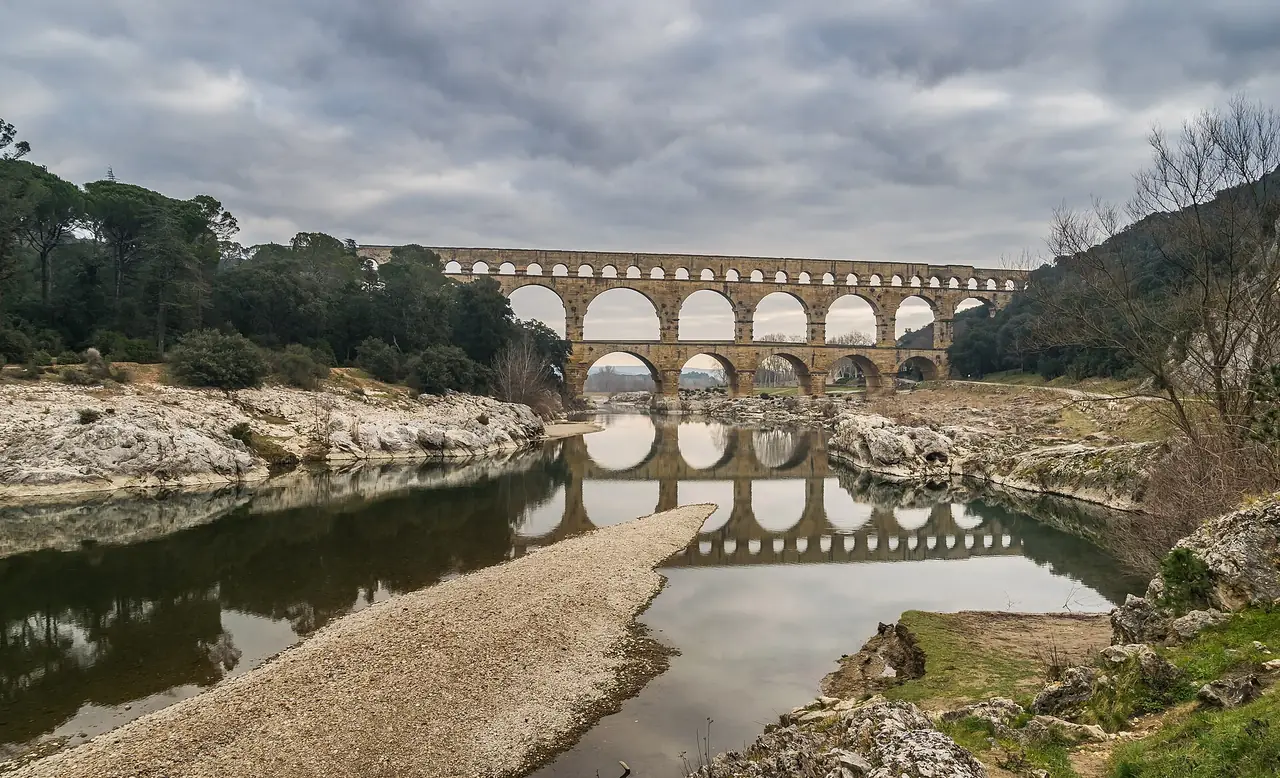 สะพานโรมัน Pont du Gard ข้ามแม่น้ำ Gardon มองจากฝั่งหินกรวดในวันฟ้าครึ้ม ภาพจาก Wikimedia Commons ผู้ถ่าย Krzysztof Golik สัญญา CC BY-SA 4.0