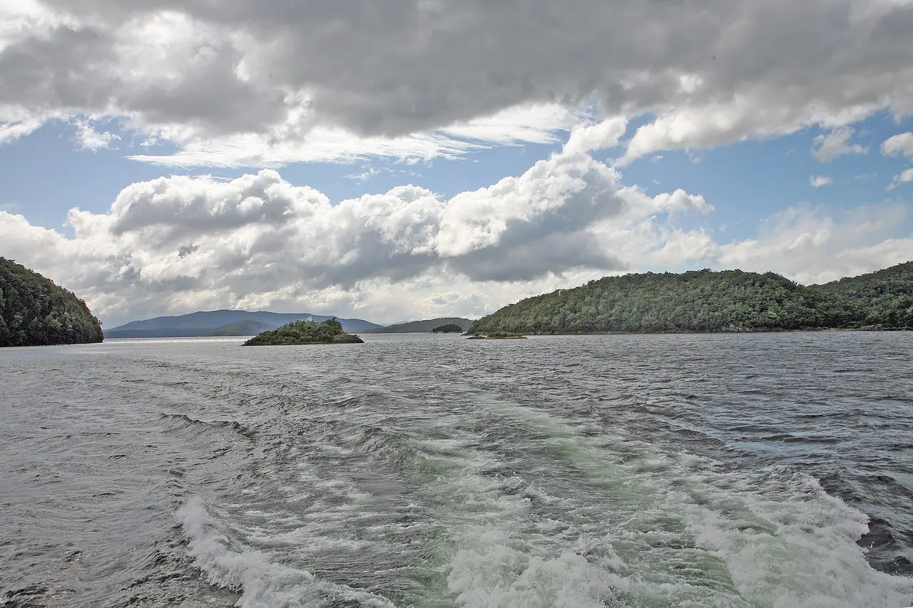 ผืนน้ำของทะเลสาบ Manapouri มองจากเรือ มีเกาะเล็กและคลื่นท้ายเรือ ภาพจาก Wikimedia Commons ผู้ถ่าย W. Bulach สัญญา CC BY-SA 4.0