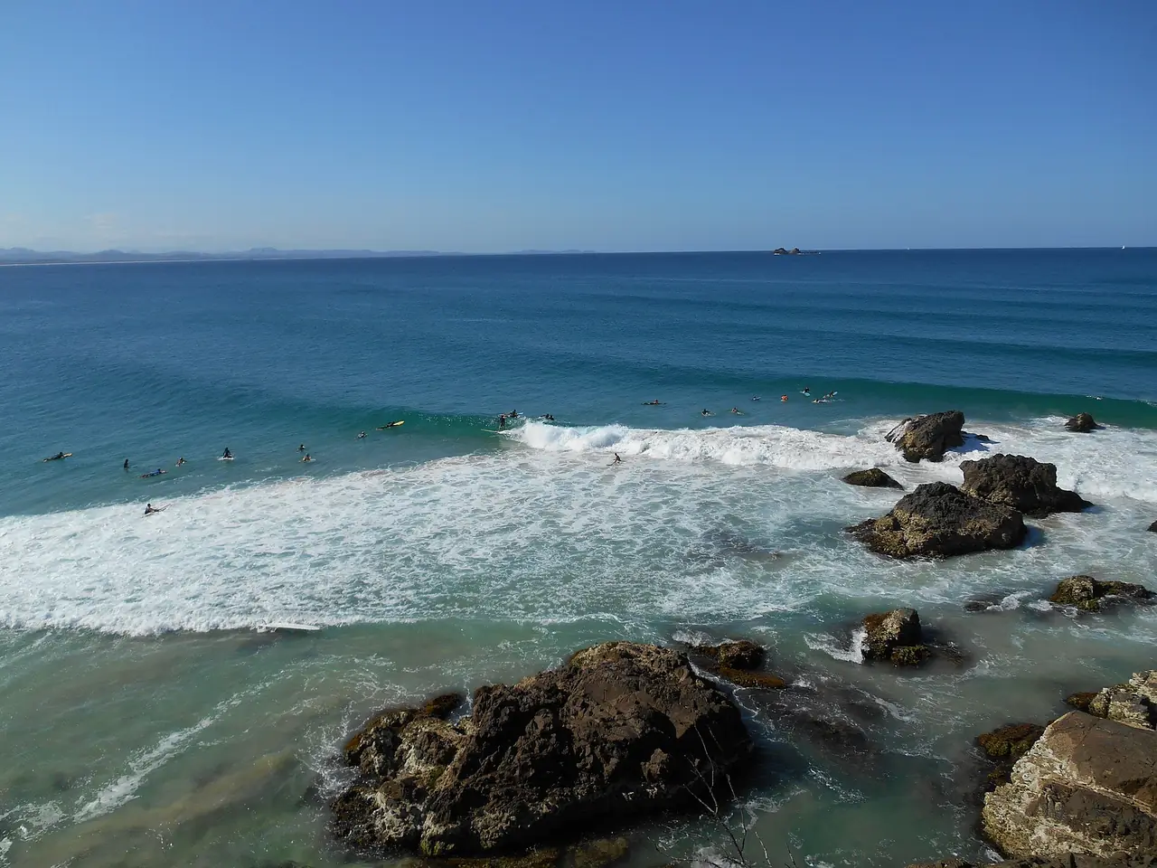 คลื่นซัดหินและนักเล่นเซิร์ฟกลุ่มเล็กที่เขต Cape Byron Marine Protected Area ภาพจาก Wikimedia Commons ผู้ถ่าย Richhandley สัญญา CC BY-SA 4.0 ภาพเก่า ไม่ทราบปีถ่าย