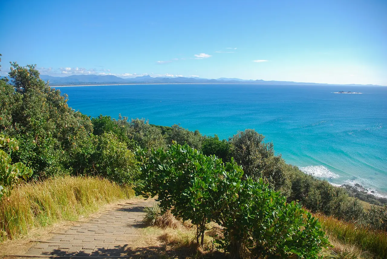 ทางเดินปูอิฐที่นำไปสู่จุดชมวิวทะเลบน Cape Byron Walking Track เห็นอ่าวและภูเขาไกล ๆ ภาพจาก Wikimedia Commons ผู้ถ่าย Ena Music สัญญา CC BY-SA 4.0