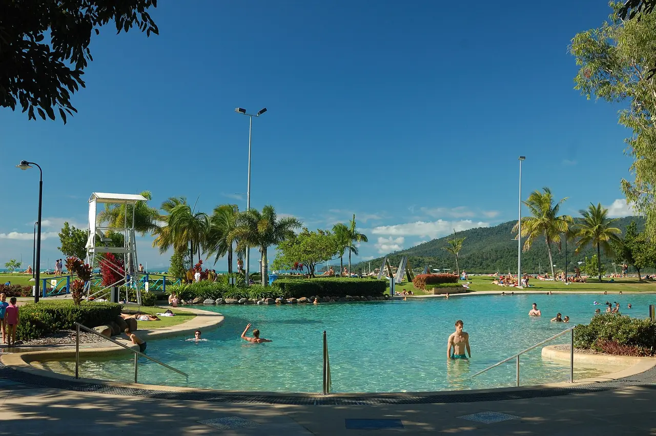 สระน้ำสาธารณะ Airlie Beach Lagoon ริมทะเลที่ Airlie Beach มีเนินเขาและต้นปาล์มเป็นฉากหลัง ภาพจาก Wikimedia Commons ผู้ถ่าย Niki Gango สัญญา CC BY-SA 3.0 ภาพเก่า ไม่ทราบปีถ่าย