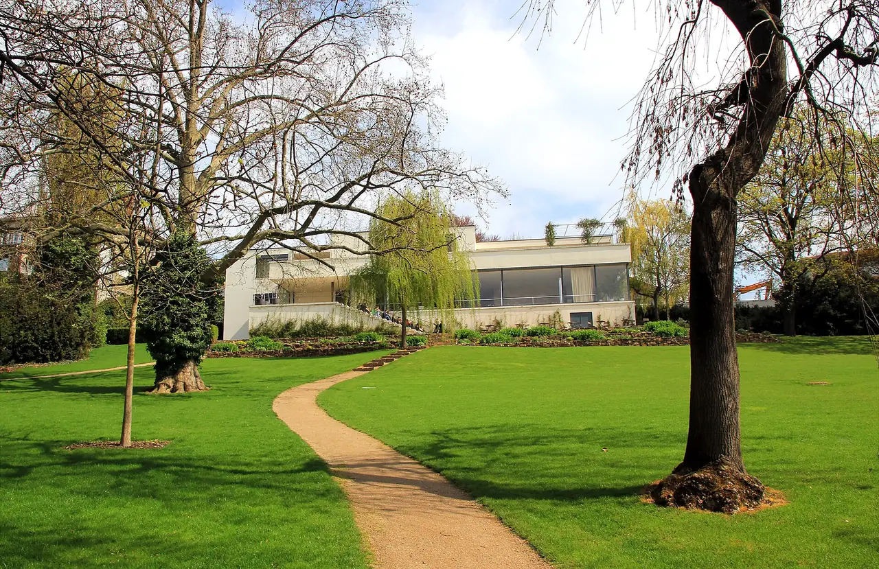 สวนและตัวบ้านวิลลา Tugendhat มองจากสนามหญ้าในเดือนที่ต้นไม้เริ่มผลิใบ ภาพจาก Wikimedia Commons ผู้ถ่าย Karelj สัญญา CC BY-SA 3.0 ถ่ายปี 2016 ตามชื่อไฟล์