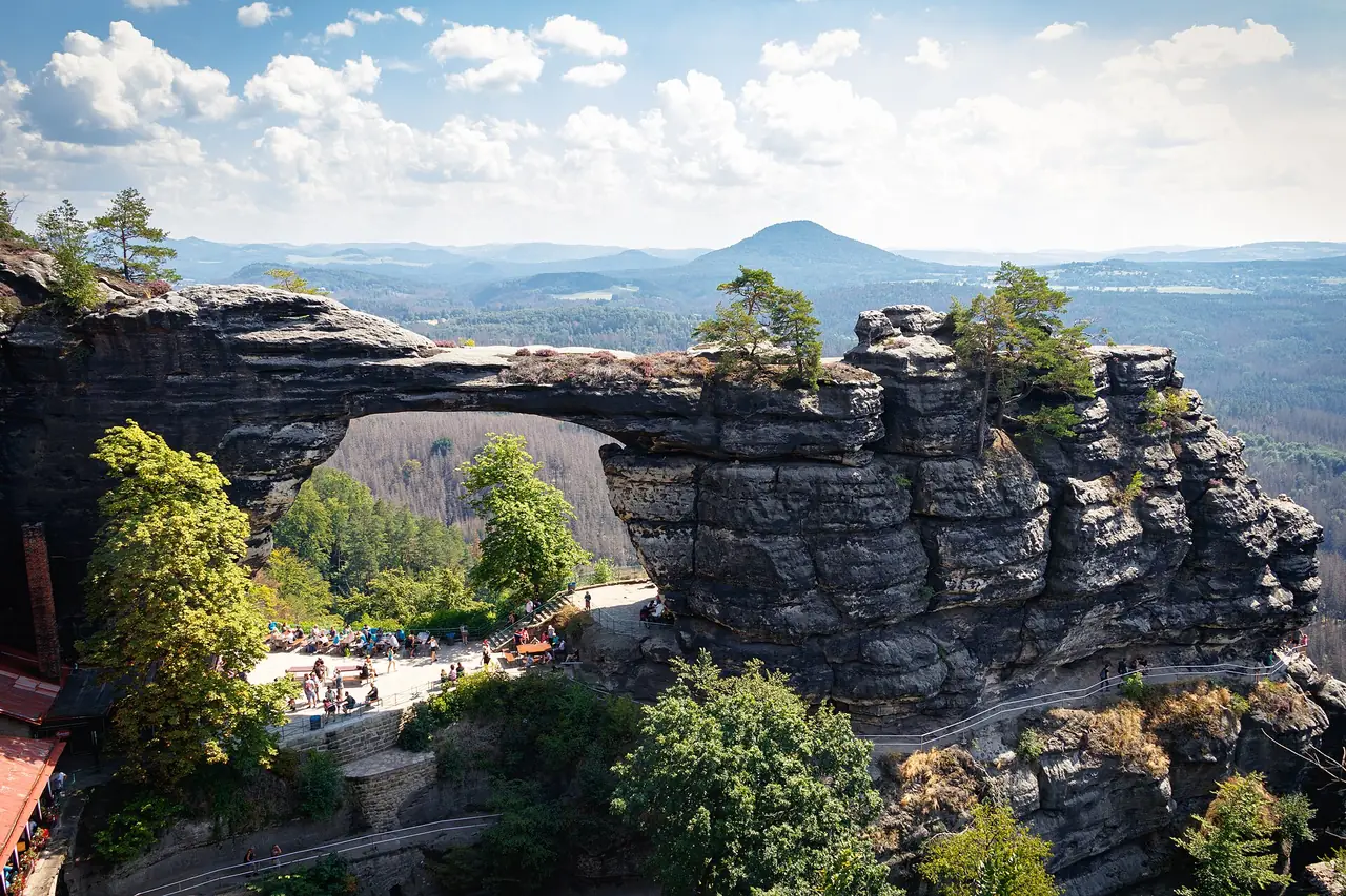 ประตูหิน Pravčická เห็นผู้คนที่ลานด้านล่างและภูเขาไกลๆ ภาพจาก Wikimedia Commons ผู้ถ่าย Zrzek007 สัญญา CC BY-SA 4.0 ถ่ายวันที่ 17 ส.ค. 2020 ตามชื่อไฟล์