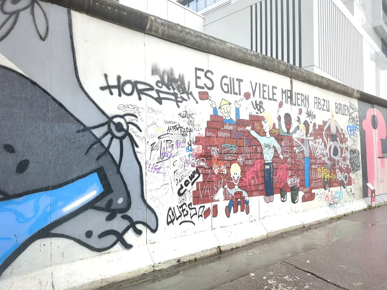 ช่วงกำแพง East Side Gallery ด้านหน้าที่ถ่ายเดือน ม.ค. 2568 เห็นภาพการ์ตูนกำแพงอิฐและคำเขียนกราฟฟิตีทับ ภาพจาก Wikimedia Commons ผู้ถ่าย C.Suthorn สัญญา CC BY-SA 4.0
