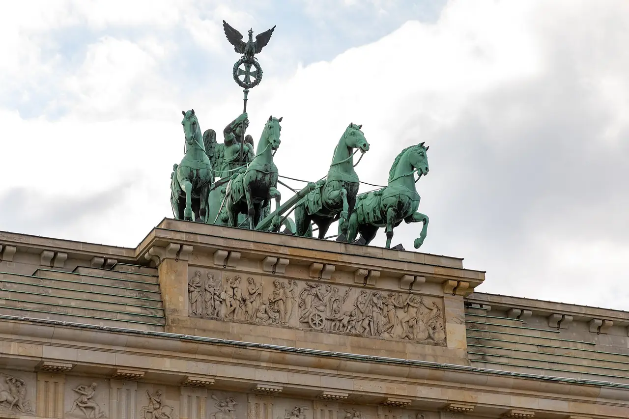 ส่วนบนของประตูบรันเดนบวร์กพร้อมรูปปั้น Quadriga และภาพนูนต่ำใต้ฐาน ภาพจาก Wikimedia Commons ผู้ถ่าย Dietmar Rabich สัญญา CC BY-SA 4.0 ปีที่ถ่าย 2562