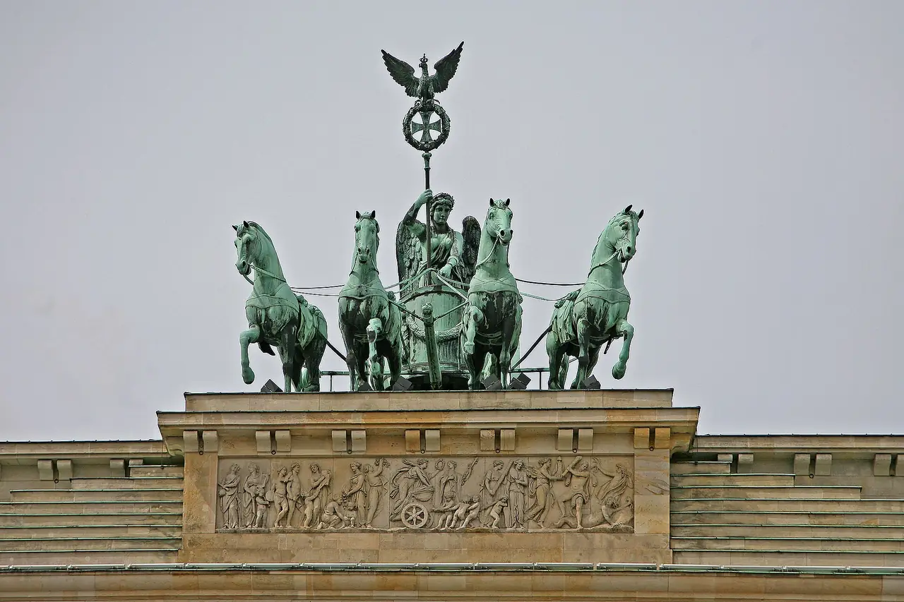รูปปั้น Quadriga บนยอดประตูบรันเดนบวร์ก ม้าสี่ตัวและเทพีแห่งชัยชนะ ภาพจาก Wikimedia Commons ผู้ถ่าย W. Bulach สัญญา CC BY-SA 4.0 ปีที่ถ่ายไม่ระบุ ภาพนี้เป็นมุมซูมที่ไม่เห็นตัวประตูทั้งหลัง