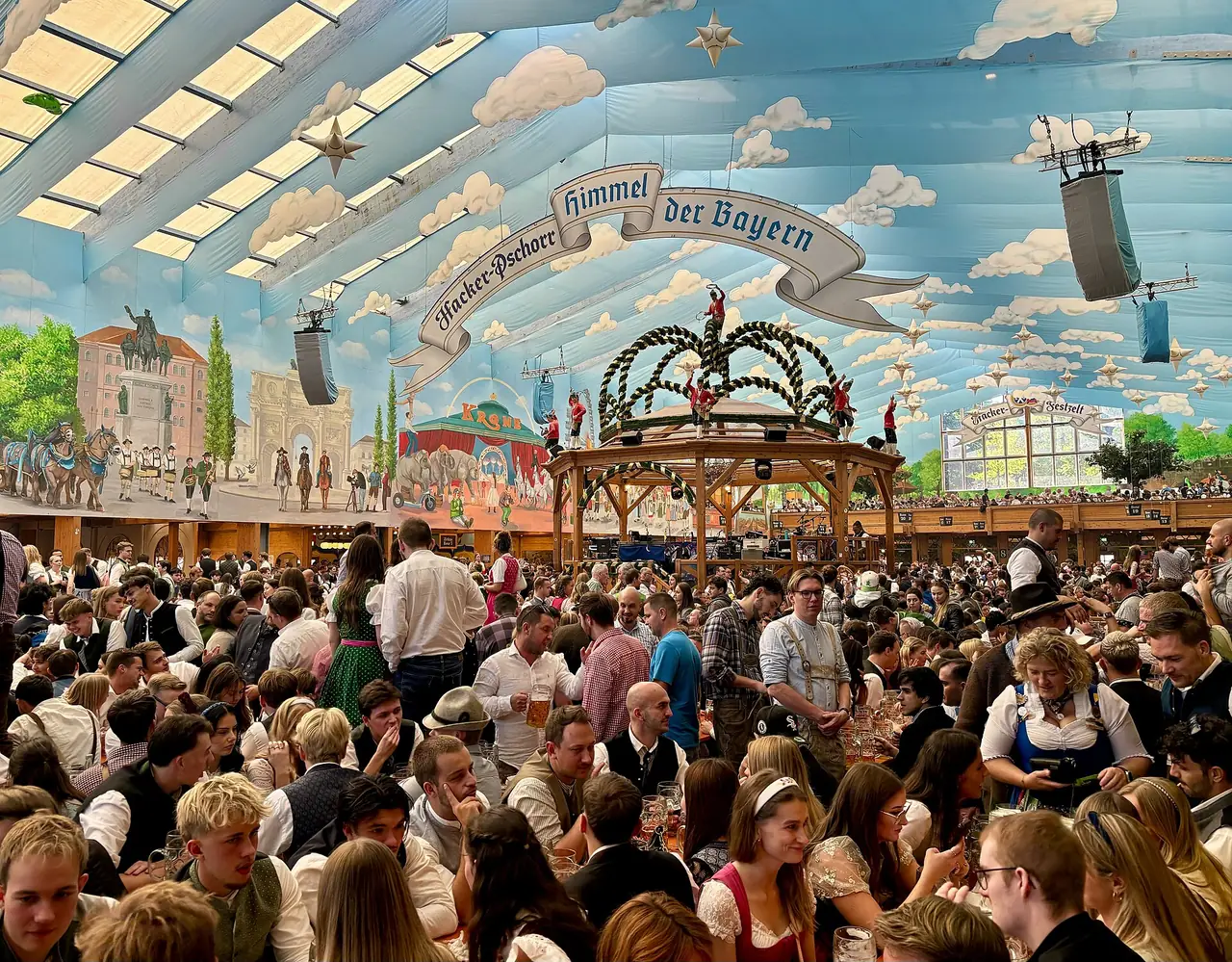 ภายในเต็นท์ Hacker-Festzelt ที่งาน Oktoberfest ปี 2568 เพดานวาดท้องฟ้าและตึกเมือง ภาพจาก Wikimedia Commons ผู้ถ่าย kallerna สัญญา CC BY-SA 4.0