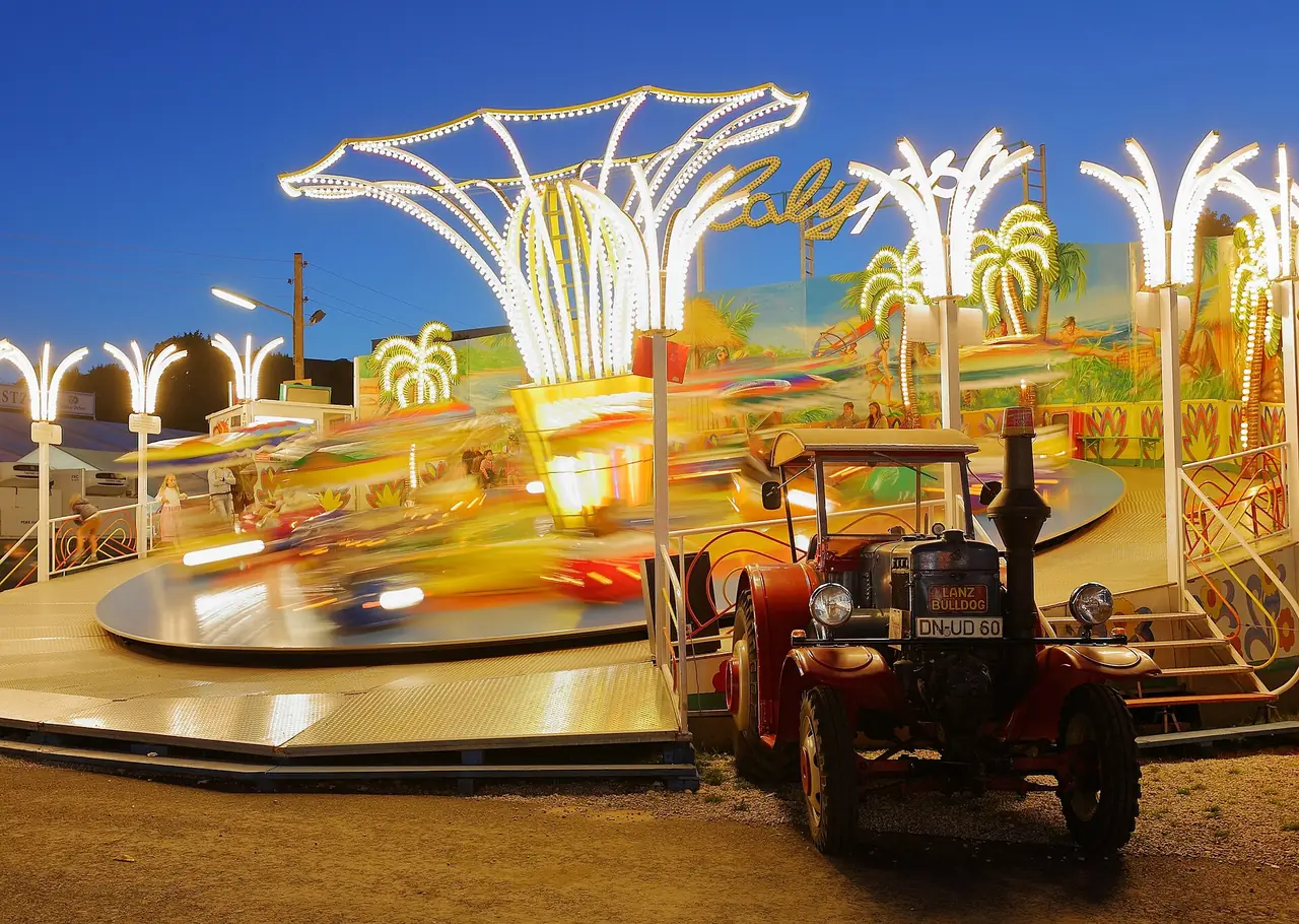 เครื่องเล่นโบราณและรถแทรกเตอร์เก่าที่ Oide Wiesn ถ่ายยามค่ำ ภาพจาก Wikimedia Commons ผู้ถ่าย Martin Falbisoner สัญญา CC BY-SA 4.0 ถ่ายปี 2558