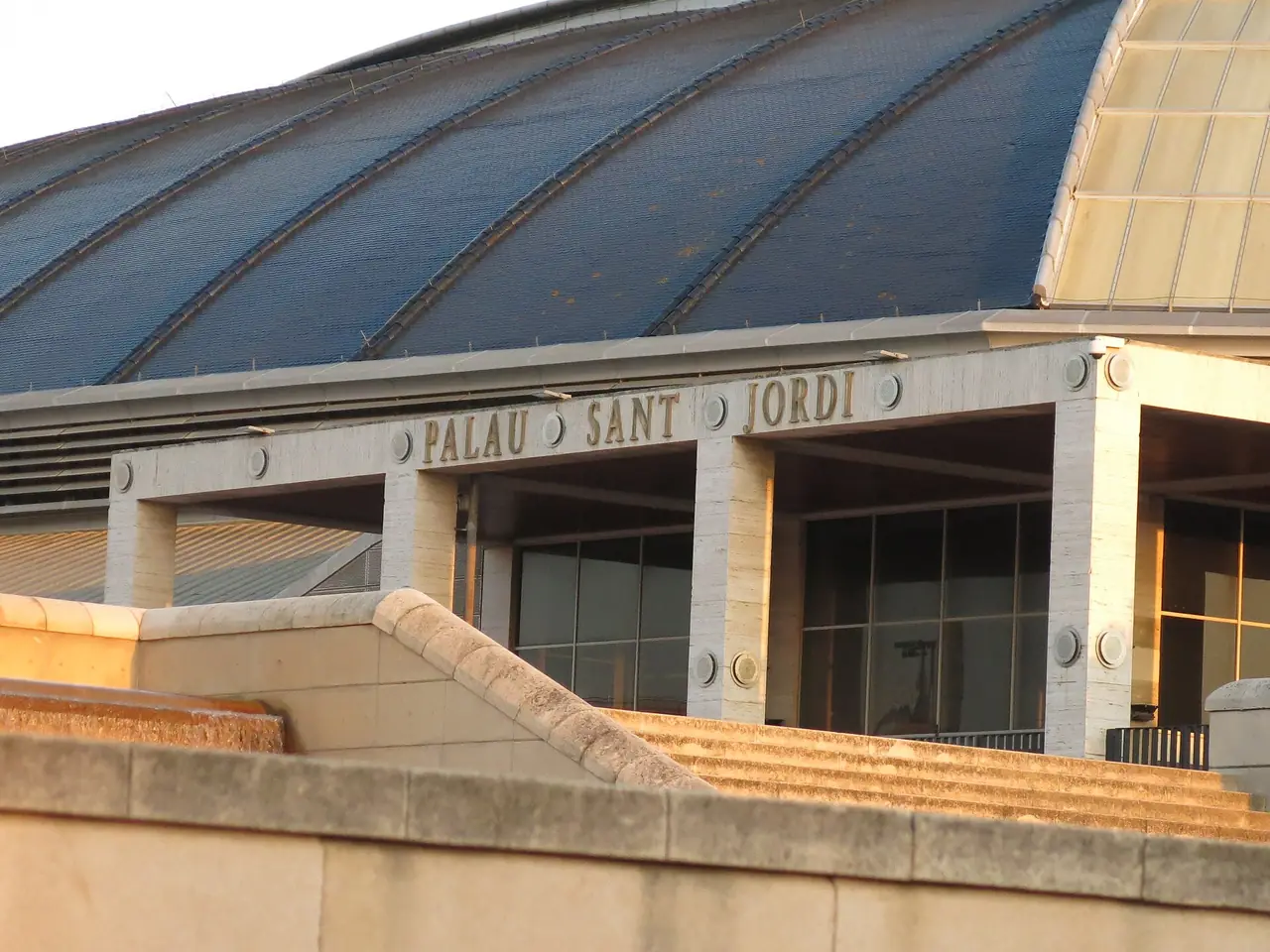 ทางเข้า Palau Sant Jordi บนอาเนลลาโอลิมปิก (Anella Olímpica) ภาพถ่ายจาก Wikimedia Commons ผู้ถ่าย Enric สัญญา CC BY-SA 4.0