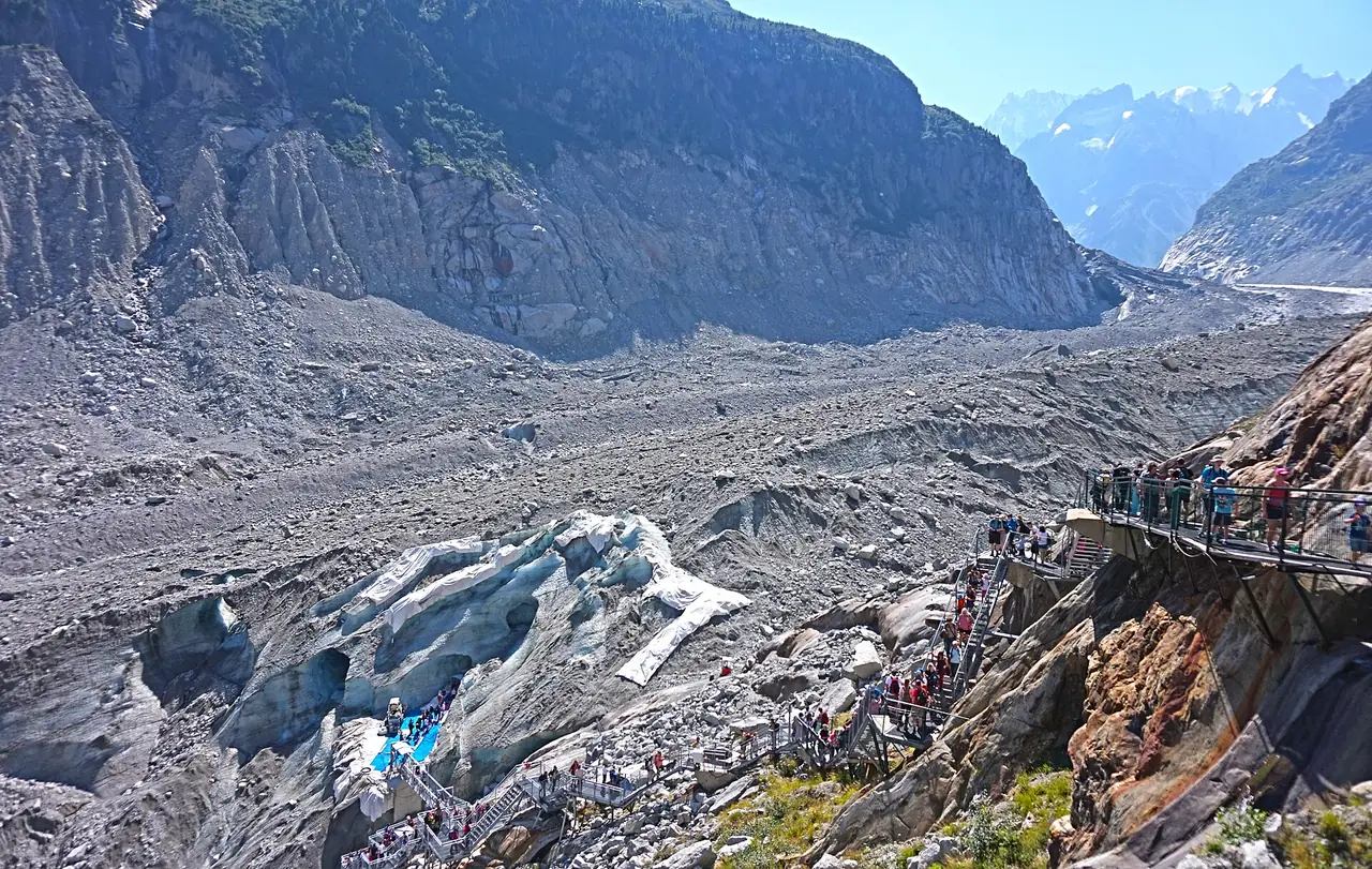 ปากถ้ำน้ำแข็งของ Mer de Glace กับนักท่องเที่ยวบนทางเดินด้านขวาของภาพ ภาพจาก Wikimedia Commons ผู้ถ่าย Tiia Monto สัญญา CC BY-SA 3.0