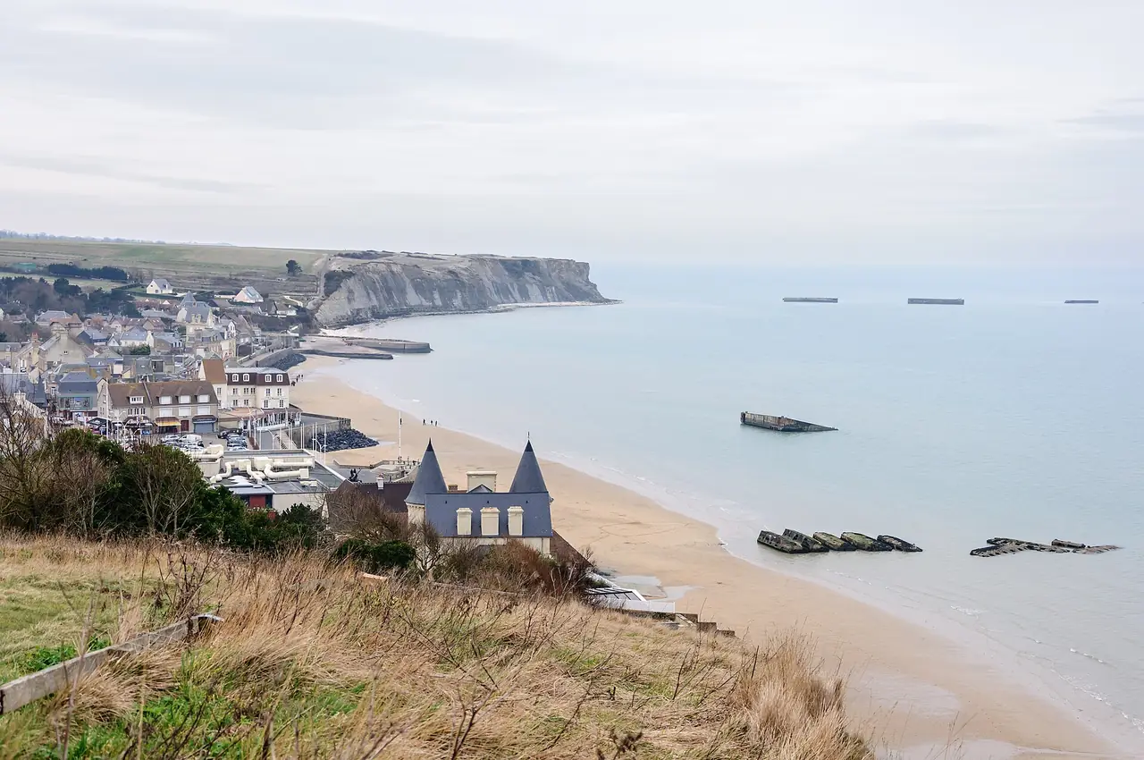 เมือง Arromanches-les-Bains และชายหาดมองจากหน้าผา เห็นซากท่าเรือเทียม Mulberry ในน้ำ ภาพจาก Wikimedia Commons ผู้ถ่าย Myrabella สัญญา CC BY-SA 3.0