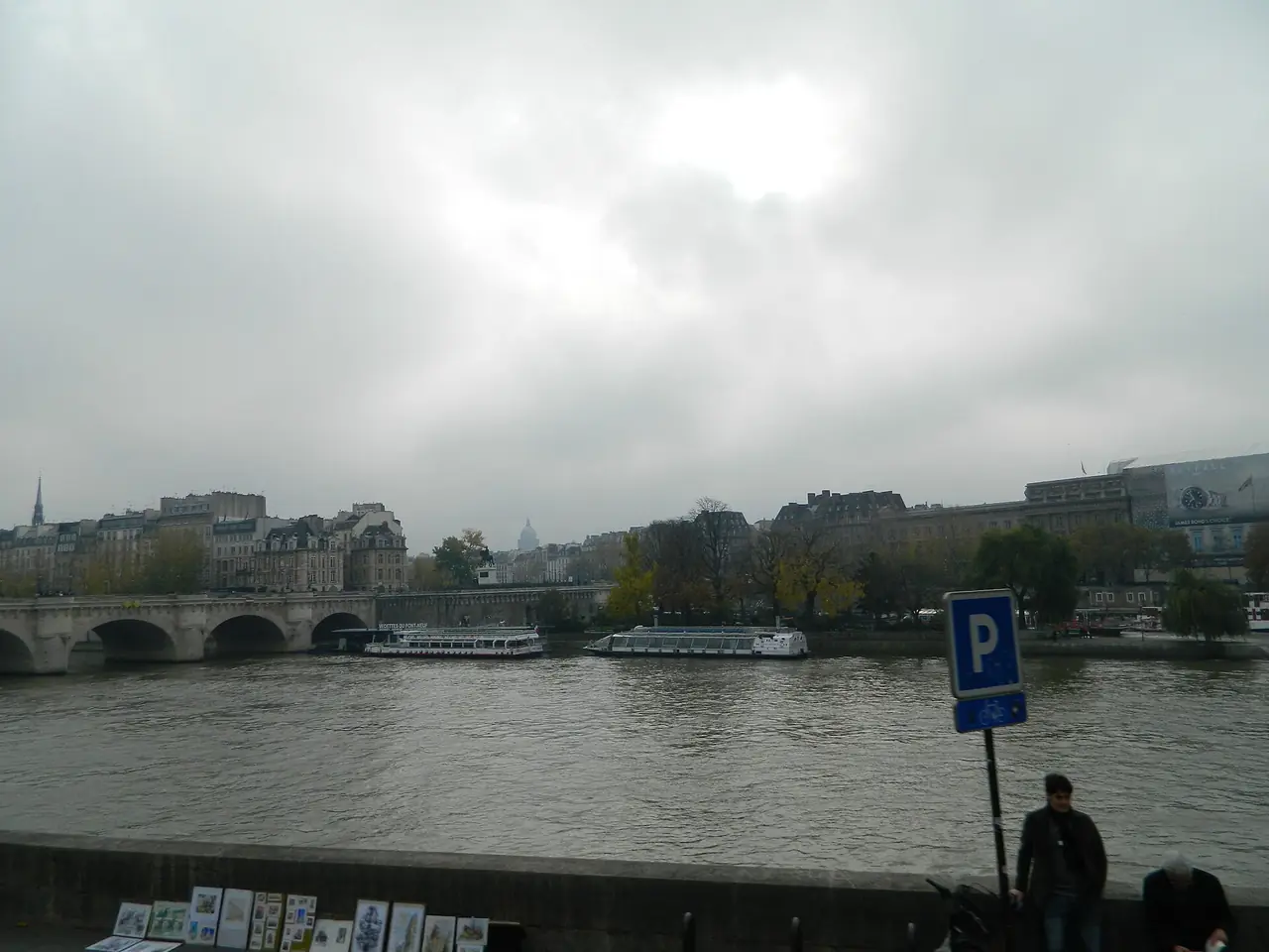 ริมแม่น้ำแซนใกล้ท่า Vedettes du Pont-Neuf วันฟ้าครึ้ม ภาพนี้เห็นน้ำและสะพานไกล ๆ ไม่ใช่ภาพเรือ ภาพจาก Wikimedia Commons ผู้ถ่าย Freepenguin สัญญา CC BY-SA 3.0