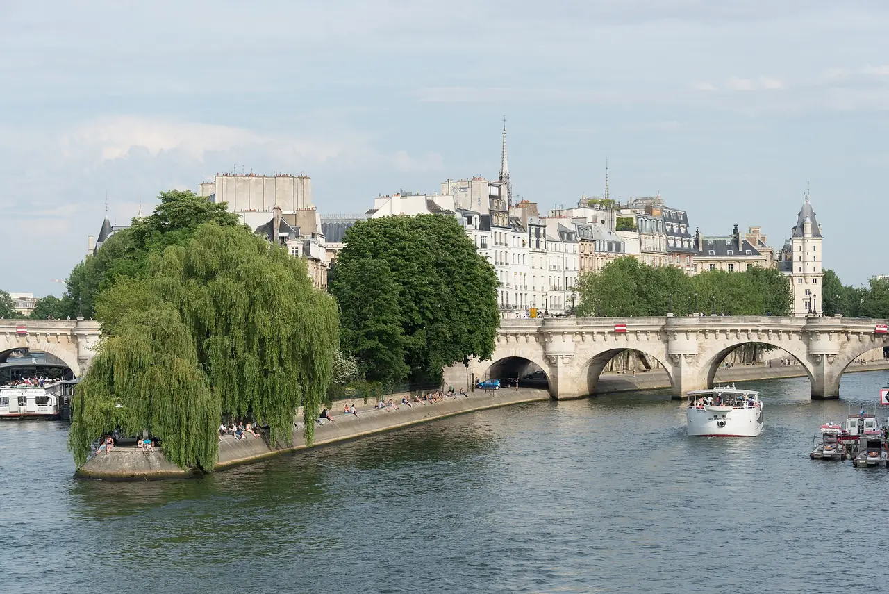 ปลายเกาะ Île de la Cité ที่ Square du Vert-Galant และสะพาน Pont Neuf มองจากริมน้ำ มีเรือท่องเที่ยวแล่นผ่าน ภาพปี 2017 จาก Wikimedia Commons ผู้ถ่าย xiquinhosilva สัญญา CC BY 2.0