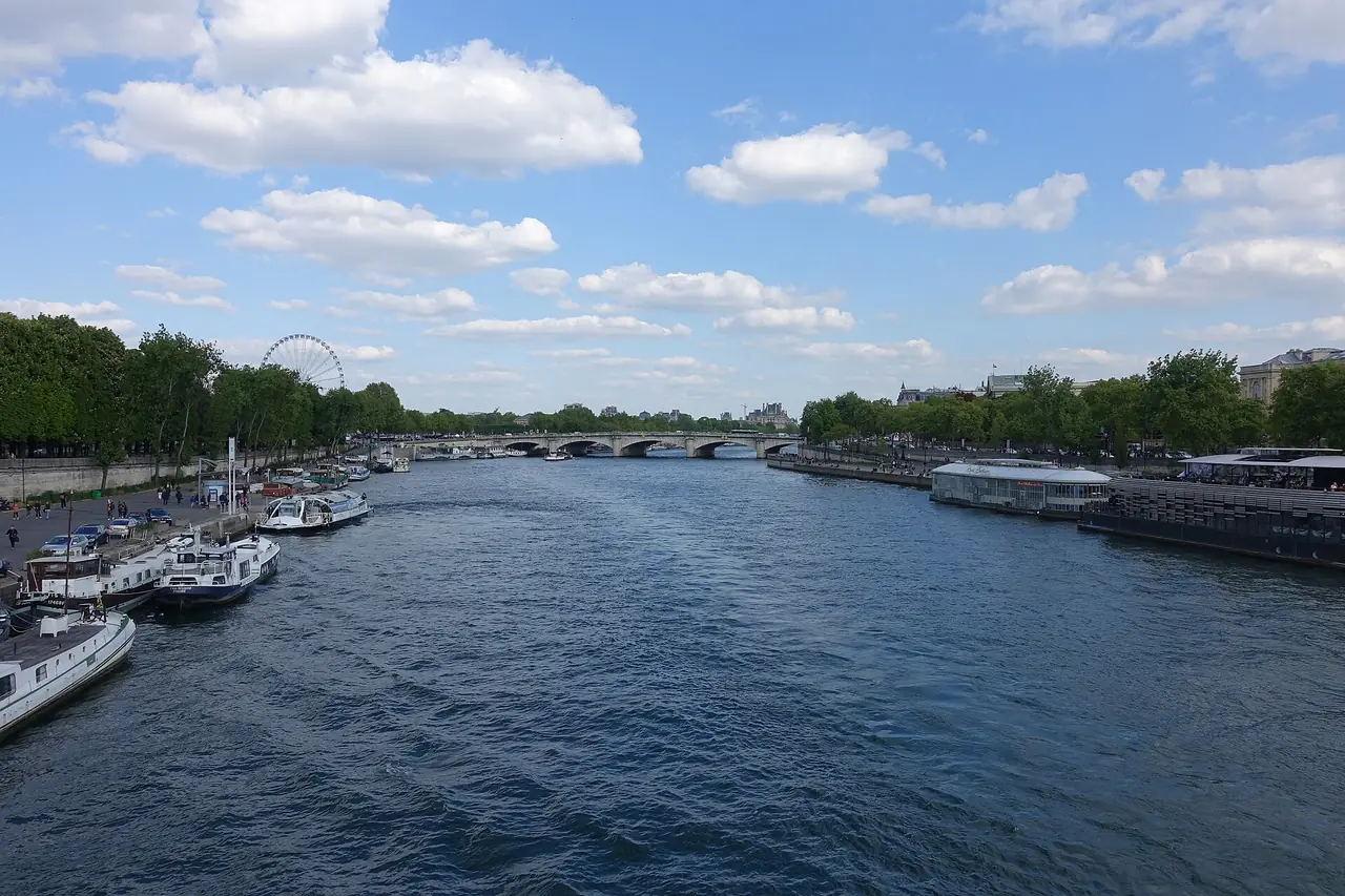 แม่น้ำแซนมองจาก Pont Alexandre III ท้องฟ้าแจ่มใส มีเรือจอดทั้งสองฝั่งและชิงช้าสวรรค์ไกล ๆ ภาพจาก Wikimedia Commons ผู้ถ่าย Guilhem Vellut สัญญา CC BY 2.0