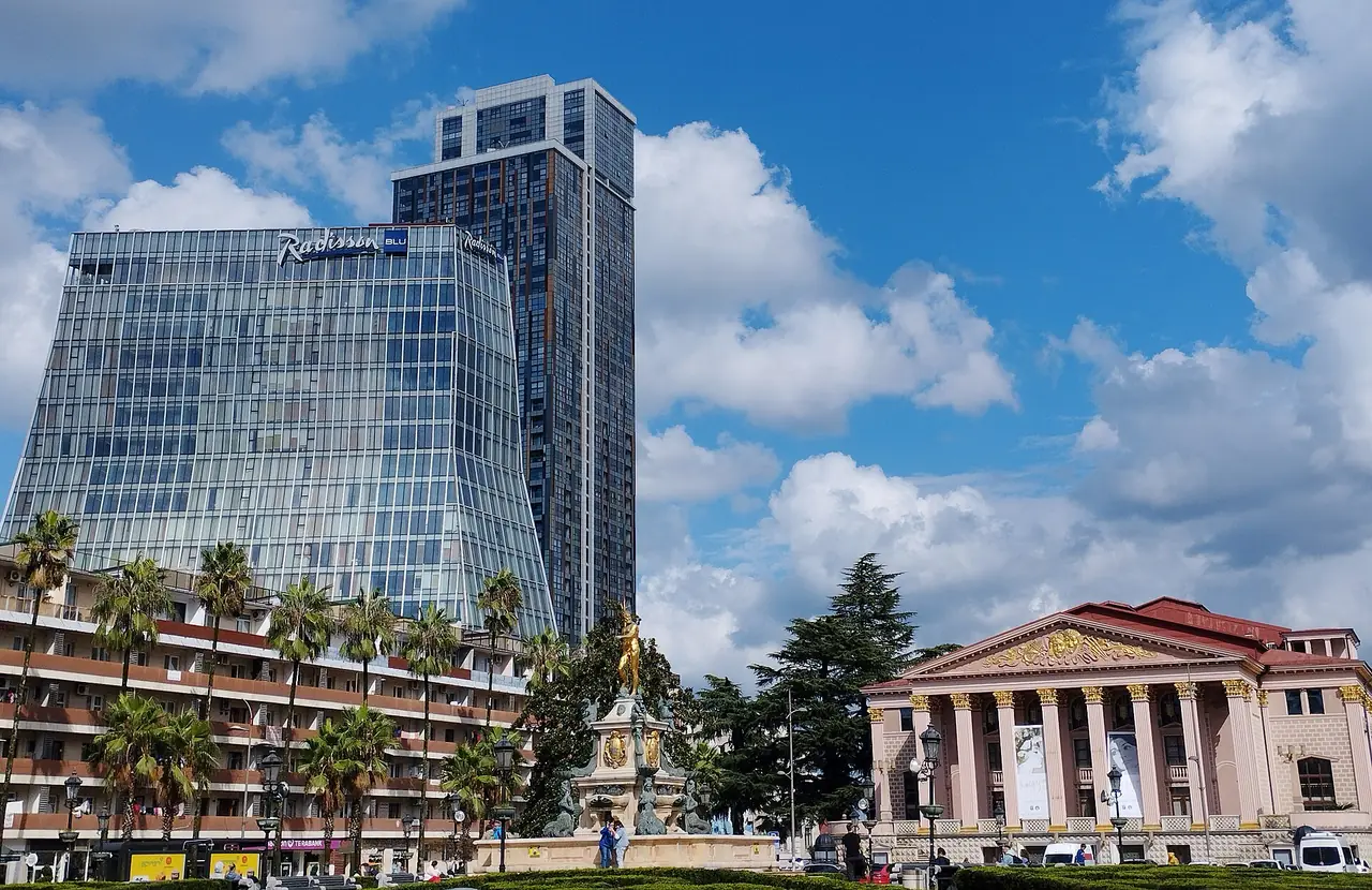 ตึกกระจกมีป้าย Radisson ข้างโรงละครและน้ำพุกลางเมืองบาทูมี ภาพจาก Wikimedia Commons ผู้ถ่าย Erez.Gt สัญญา CC BY-SA 4.0