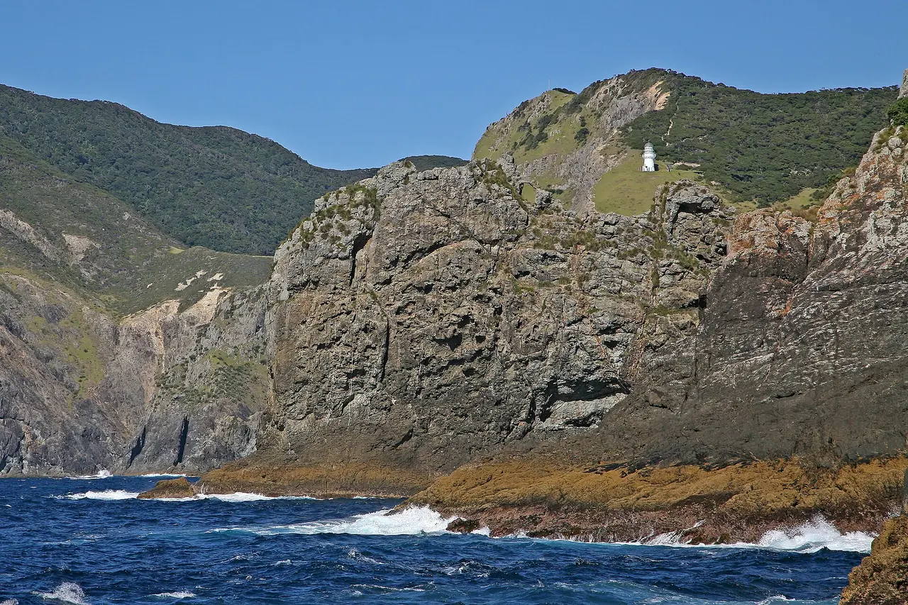 หน้าผาและประภาคาร Cape Brett บนแหลมที่เรือล่องผ่านก่อนถึง Hole in the Rock ภาพจาก Wikimedia Commons ผู้ถ่าย W. Bulach สัญญา CC BY-SA 4.0 ไม่ระบุปี