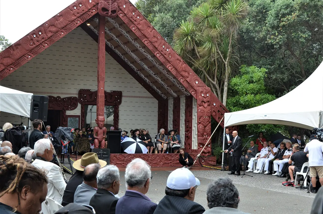 บ้านประชุม Te Whare Rūnanga ที่ Waitangi ระหว่างพิธีที่มีผู้คนเข้าร่วม ภาพจาก Wikimedia Commons ผู้ถ่าย New Zealand Government Office of the Governor-General สัญญา CC BY 4.0 ไม่ระบุปี