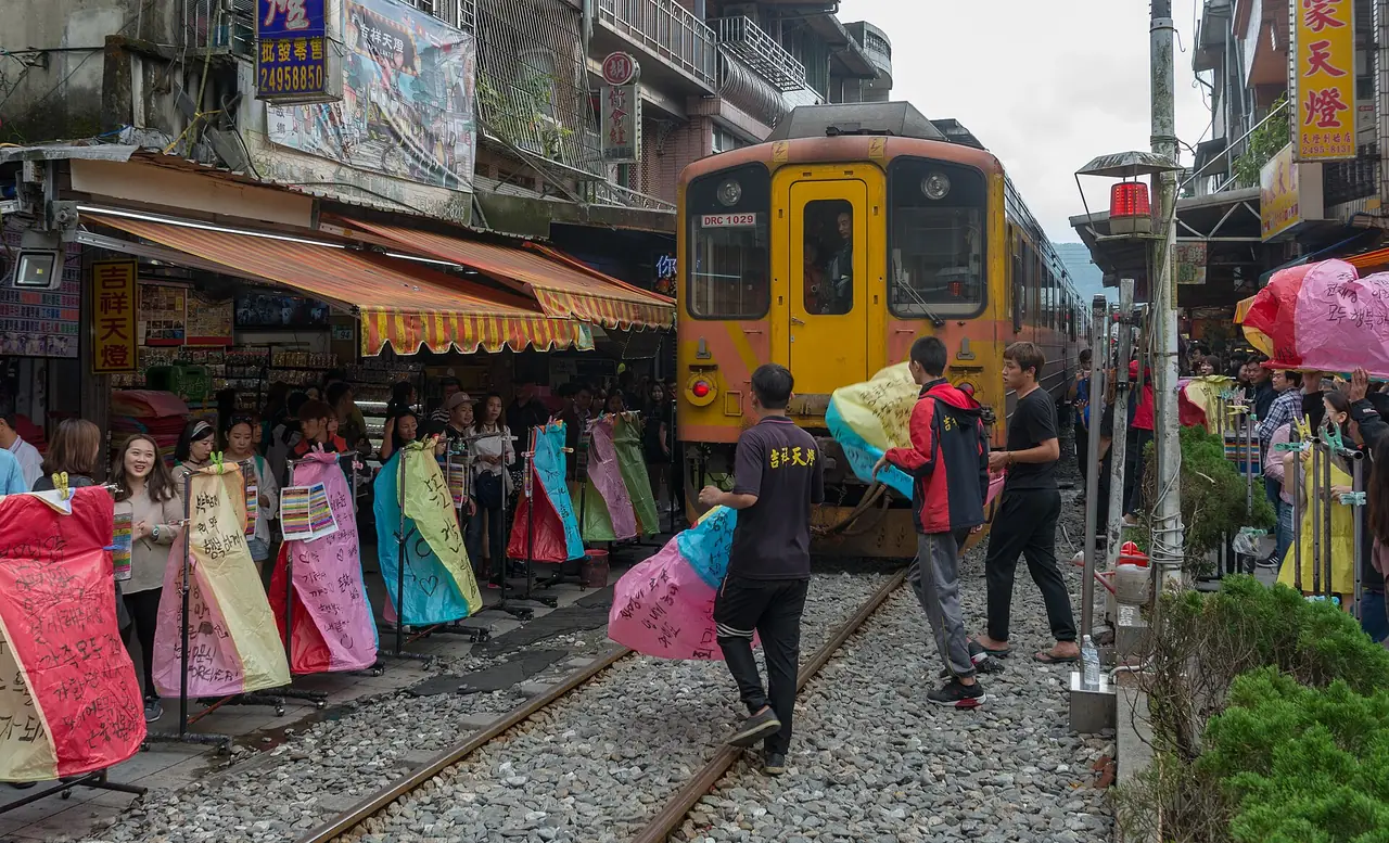 รถไฟวิ่งผ่านตรอกสือเฟินที่มีคนยืนถือโคมลอยอยู่ข้างราง