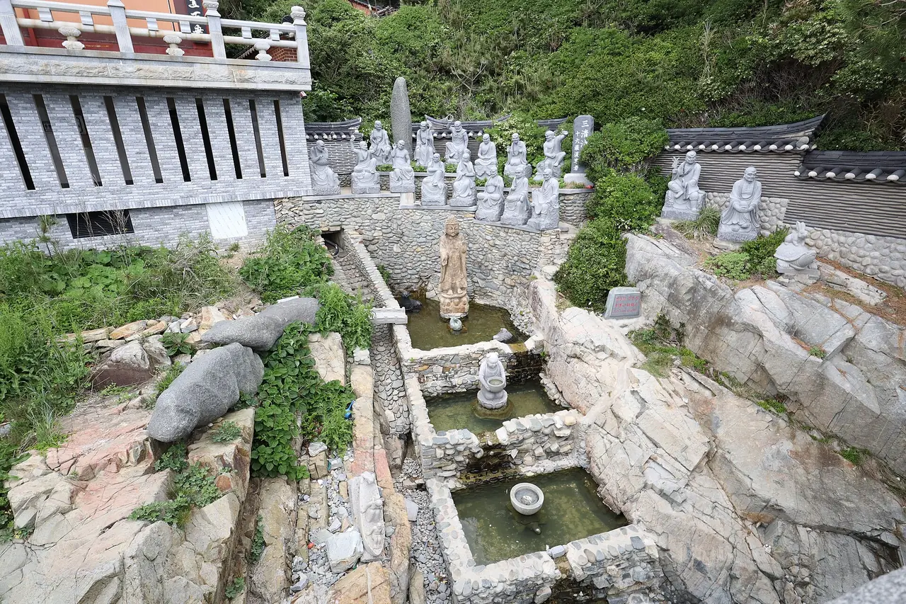 ลานหินที่มีบ่อน้ำเล็กและรูปปั้นหินเรียงตามแนวหินริมทะเลในเขตวัด